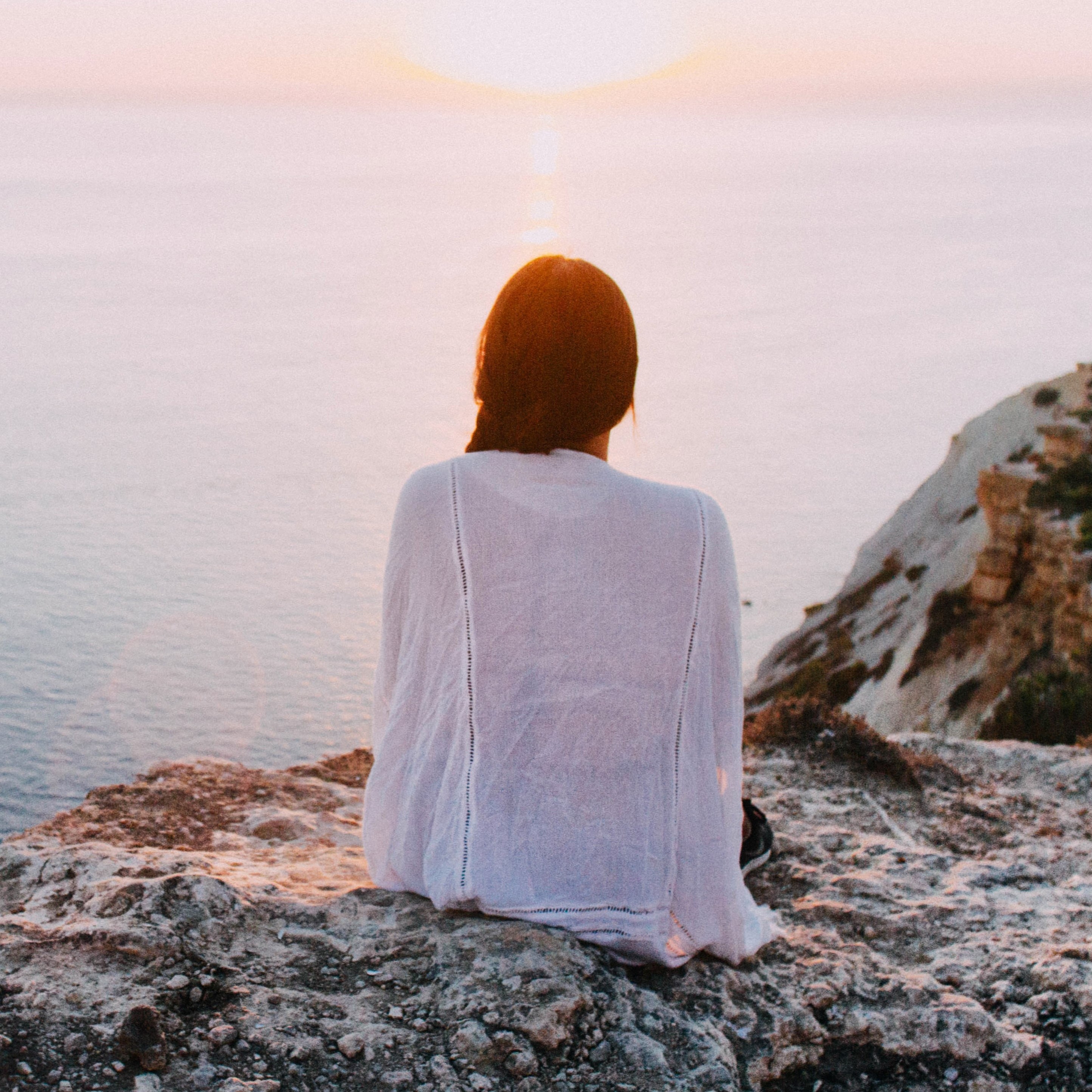 A woman peacefully sitting on the edge of a cliff overlooking the ocean.